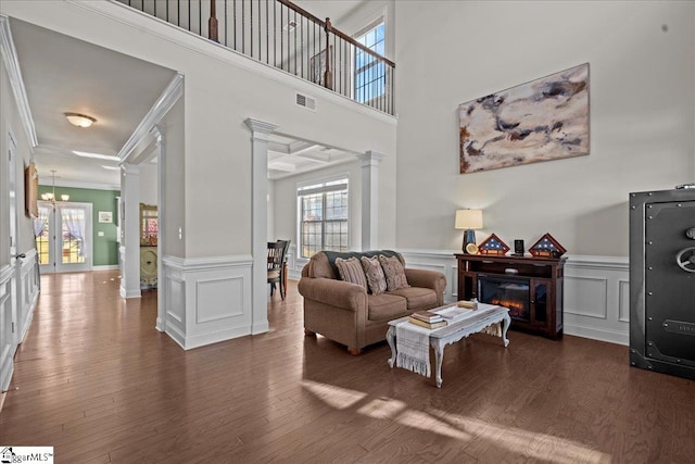 living room featuring a towering ceiling, dark hardwood / wood-style flooring, ornate columns, ornamental molding, and a chandelier