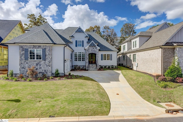 french country home featuring stone siding, a shingled roof, and a front lawn