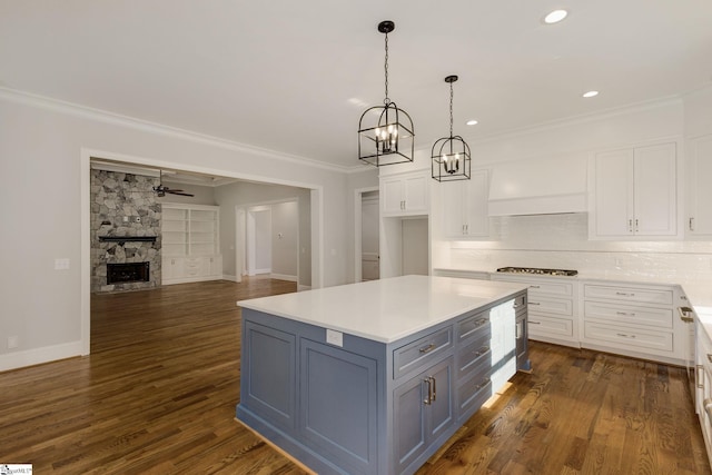 kitchen with dark wood finished floors, crown molding, a stone fireplace, white cabinetry, and gas cooktop