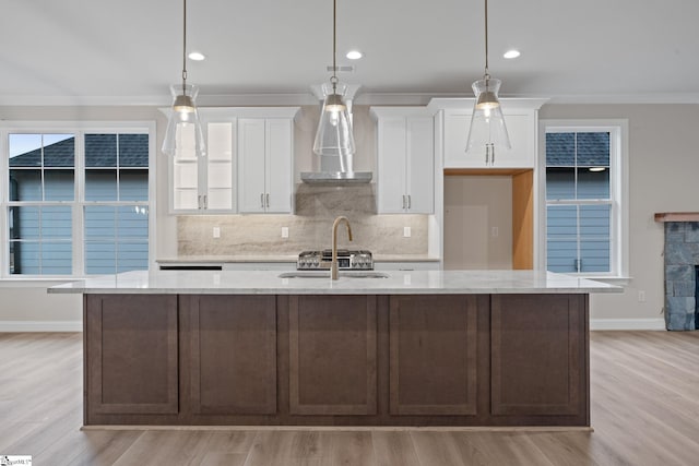 kitchen with white cabinetry, a center island with sink, light wood-type flooring, ornamental molding, and pendant lighting