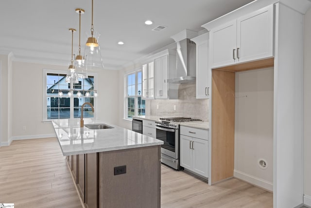 kitchen with white cabinetry, sink, wall chimney range hood, stainless steel gas range oven, and decorative light fixtures