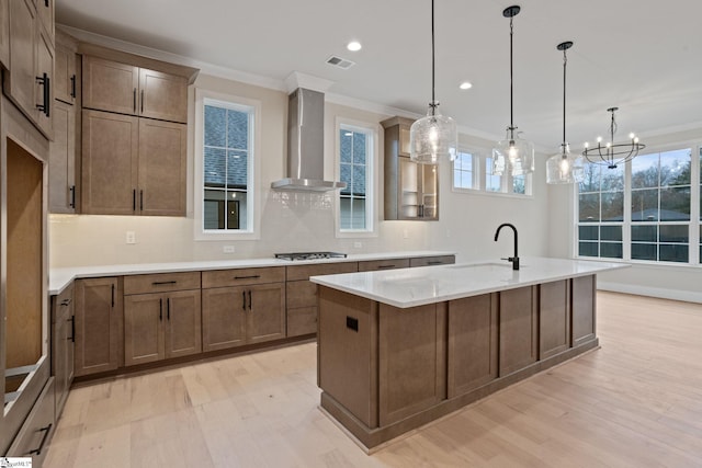 kitchen with a center island with sink, wall chimney exhaust hood, hanging light fixtures, and gas cooktop