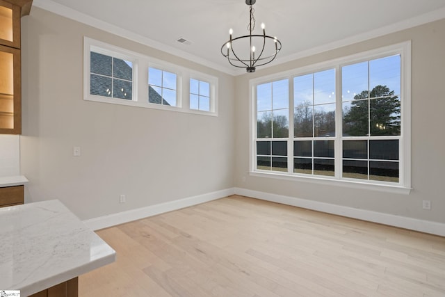 unfurnished dining area with a wealth of natural light, crown molding, light hardwood / wood-style floors, and an inviting chandelier