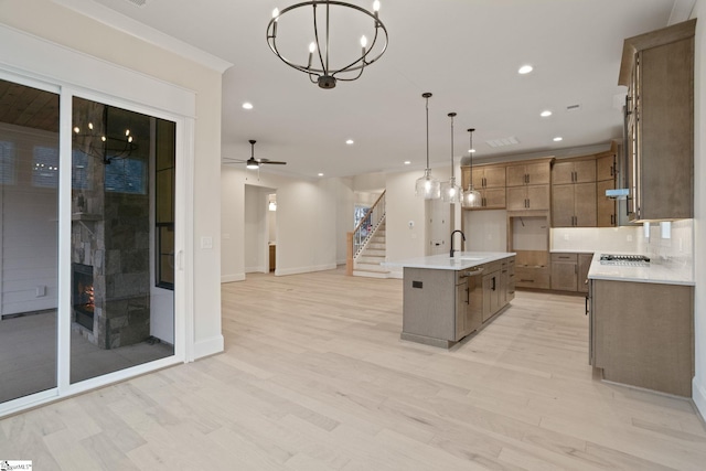 kitchen featuring a center island with sink, ceiling fan with notable chandelier, light hardwood / wood-style flooring, decorative light fixtures, and stainless steel appliances