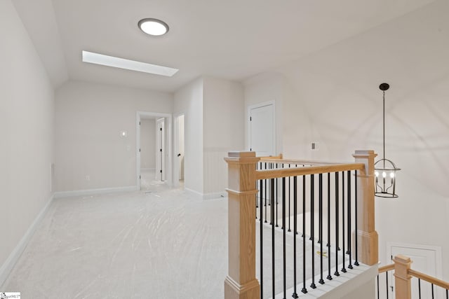 hallway featuring carpet flooring, lofted ceiling with skylight, and a notable chandelier