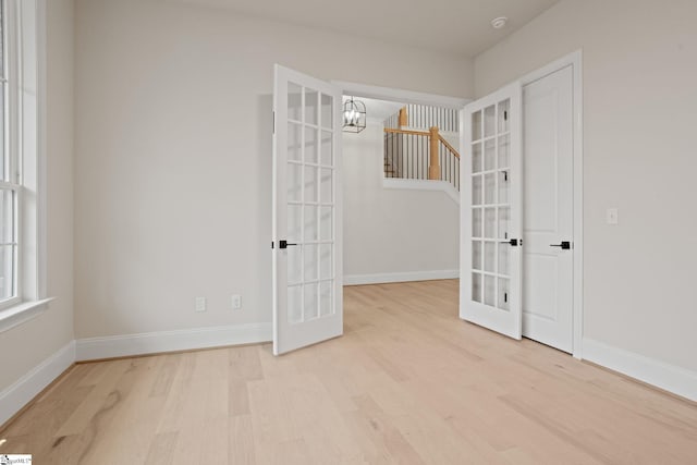 empty room with an inviting chandelier, light wood-type flooring, and french doors