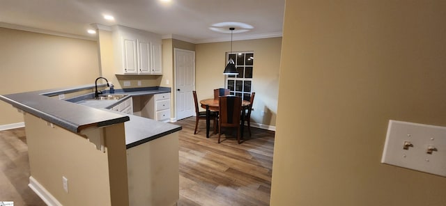 kitchen featuring hanging light fixtures, hardwood / wood-style floors, sink, white cabinets, and kitchen peninsula