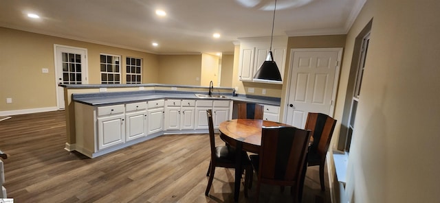 kitchen with white cabinets, hanging light fixtures, hardwood / wood-style flooring, sink, and ornamental molding