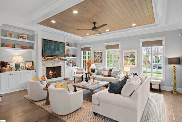 living room featuring wooden ceiling, ornamental molding, hardwood / wood-style floors, a stone fireplace, and built in features