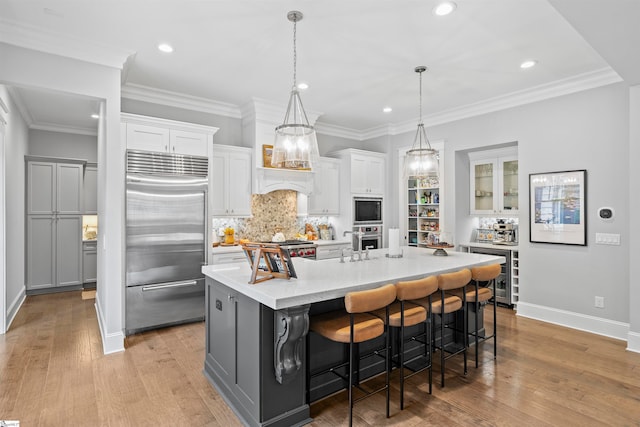 kitchen with beverage cooler, built in appliances, a kitchen island with sink, a kitchen breakfast bar, and light wood-type flooring