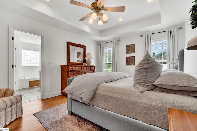 bedroom with a raised ceiling, connected bathroom, ceiling fan, and light wood-type flooring