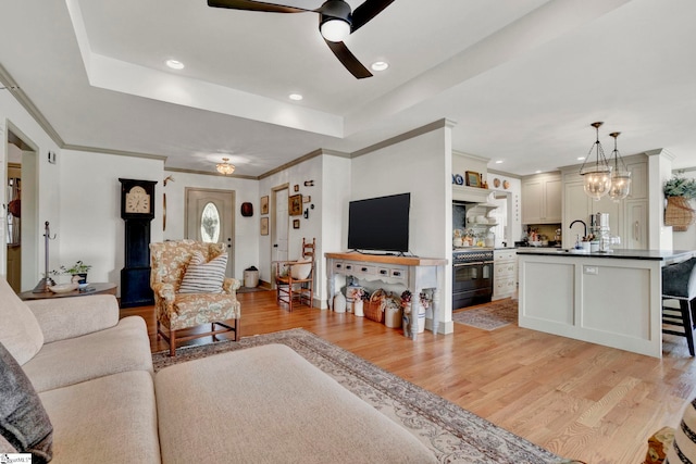 living room featuring a raised ceiling, sink, light hardwood / wood-style floors, and ceiling fan with notable chandelier