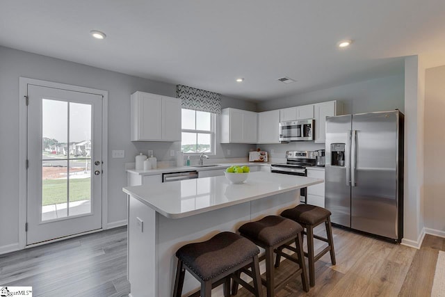 kitchen featuring appliances with stainless steel finishes, a kitchen bar, a center island, light hardwood / wood-style floors, and white cabinets