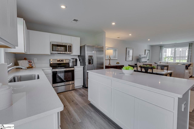 kitchen featuring sink, a center island, stainless steel appliances, white cabinets, and light hardwood / wood-style flooring