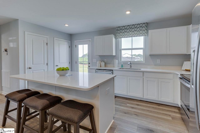 kitchen featuring sink, a center island, a breakfast bar area, white cabinets, and light hardwood / wood-style flooring