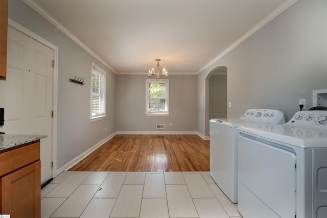 clothes washing area featuring ornamental molding, a notable chandelier, washing machine and dryer, and light wood-type flooring