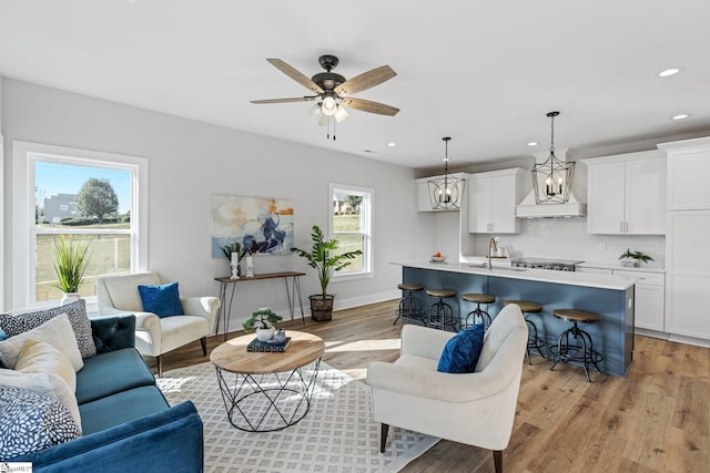 living room featuring a healthy amount of sunlight, sink, ceiling fan with notable chandelier, and light wood-type flooring