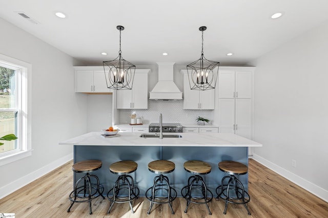 kitchen featuring a breakfast bar, premium range hood, light hardwood / wood-style floors, and an island with sink