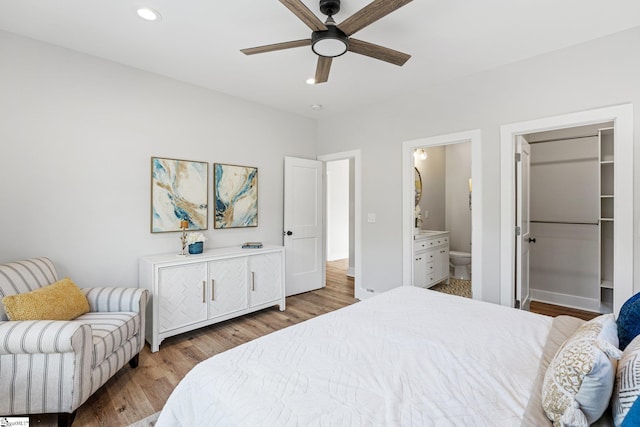 bedroom featuring a walk in closet, ensuite bath, wood-type flooring, and ceiling fan