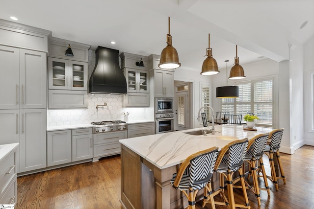 kitchen featuring dark wood-type flooring, hanging light fixtures, gray cabinetry, premium range hood, and appliances with stainless steel finishes