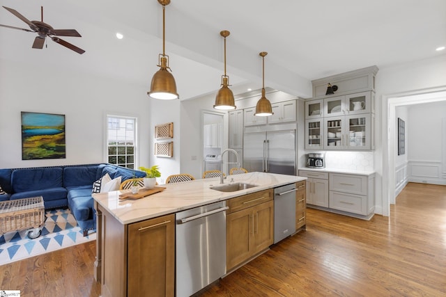 kitchen with hanging light fixtures, a center island with sink, hardwood / wood-style floors, appliances with stainless steel finishes, and light stone counters