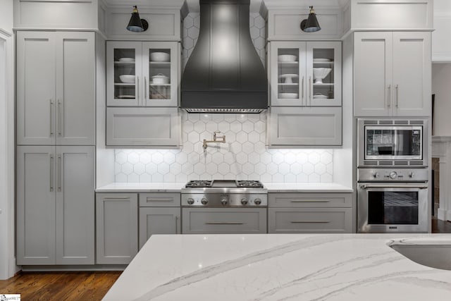 kitchen featuring gray cabinets, custom exhaust hood, light stone countertops, and stainless steel appliances