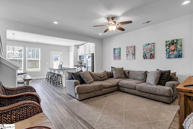 living room featuring ceiling fan with notable chandelier and light hardwood / wood-style floors