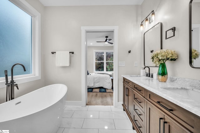 ensuite bathroom featuring a sink, double vanity, a ceiling fan, baseboards, and a soaking tub