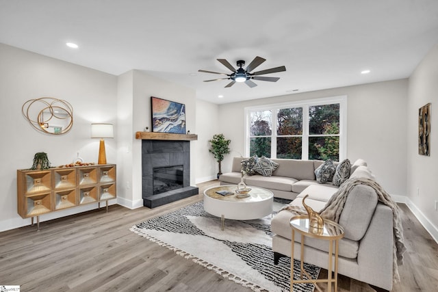 living room featuring a tiled fireplace, baseboards, recessed lighting, and wood finished floors