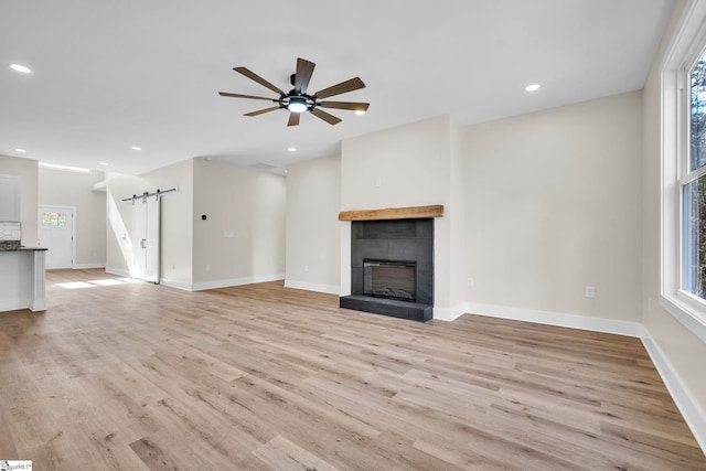 unfurnished living room featuring a healthy amount of sunlight, light hardwood / wood-style flooring, a tile fireplace, and a barn door