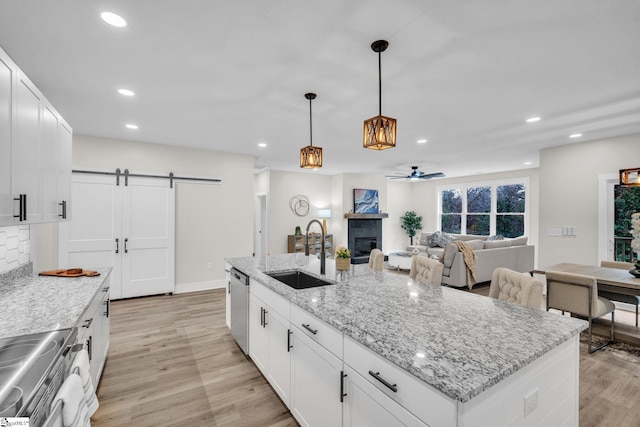 kitchen with ceiling fan, a barn door, a sink, light wood-style flooring, and appliances with stainless steel finishes