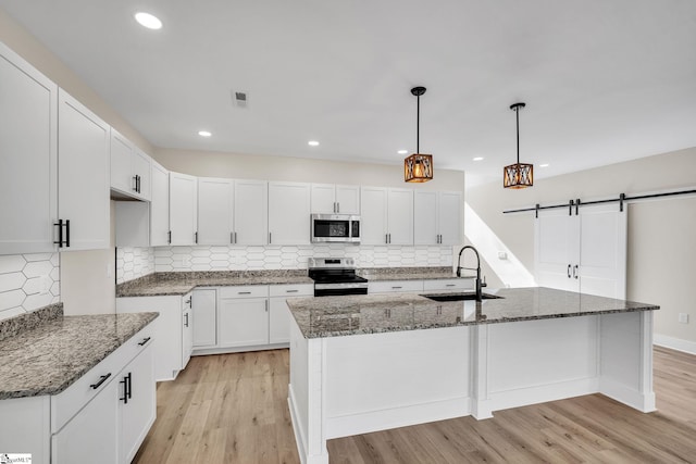 kitchen featuring a kitchen island with sink, stainless steel appliances, sink, a barn door, and light wood-type flooring