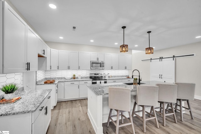kitchen featuring a barn door, a sink, white cabinets, light wood-style floors, and stainless steel appliances