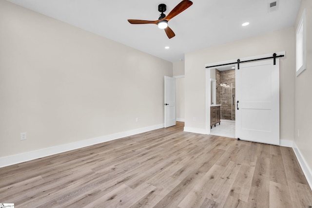 unfurnished bedroom featuring a barn door, ceiling fan, light hardwood / wood-style flooring, and ensuite bath