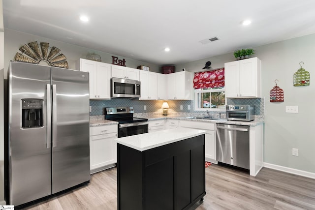 kitchen featuring a kitchen island, stainless steel appliances, backsplash, sink, and light wood-type flooring