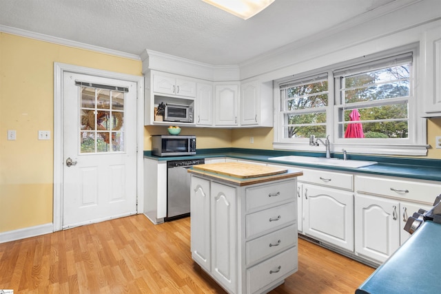 kitchen with white cabinets, a textured ceiling, light wood-type flooring, ornamental molding, and stainless steel appliances