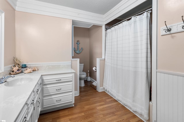 full bathroom featuring a textured ceiling, toilet, vanity, crown molding, and hardwood / wood-style flooring