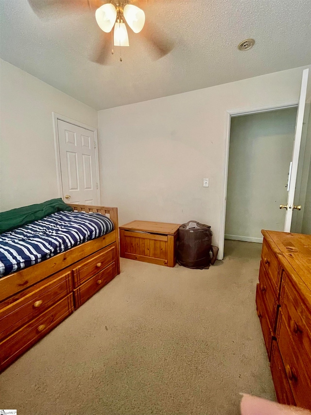 bedroom with ceiling fan, light carpet, and a textured ceiling