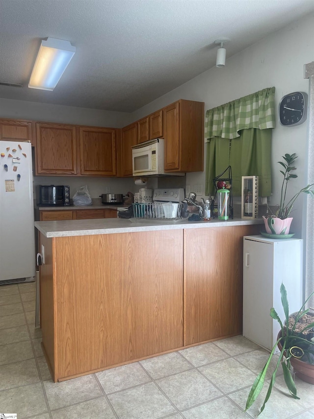 kitchen featuring white appliances, a textured ceiling, light tile patterned floors, and kitchen peninsula