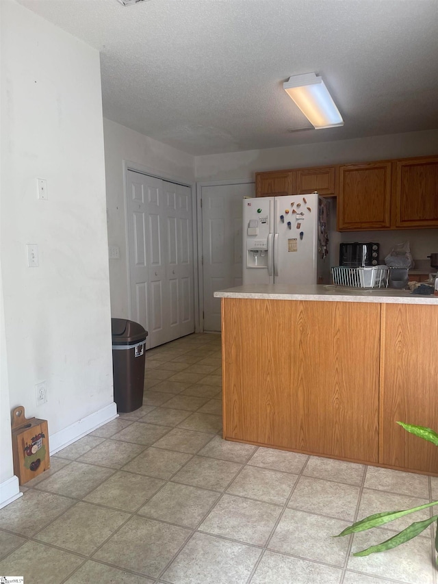 kitchen with light tile patterned flooring, a textured ceiling, white refrigerator with ice dispenser, and kitchen peninsula