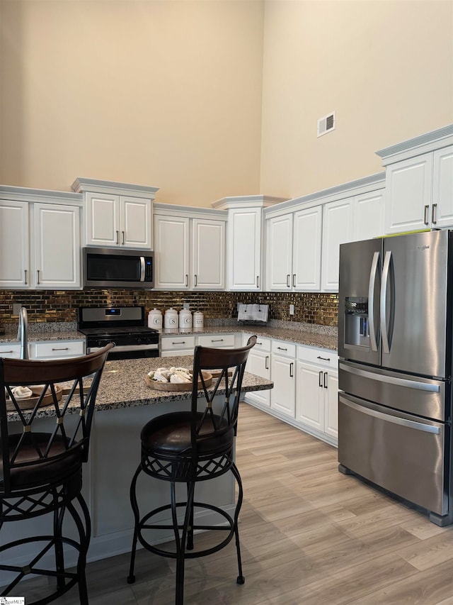 kitchen featuring a breakfast bar area, white cabinetry, dark stone countertops, a towering ceiling, and stainless steel appliances