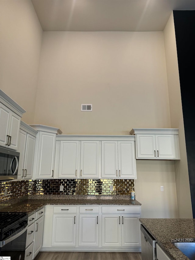 kitchen featuring white cabinetry, stainless steel appliances, and dark stone countertops