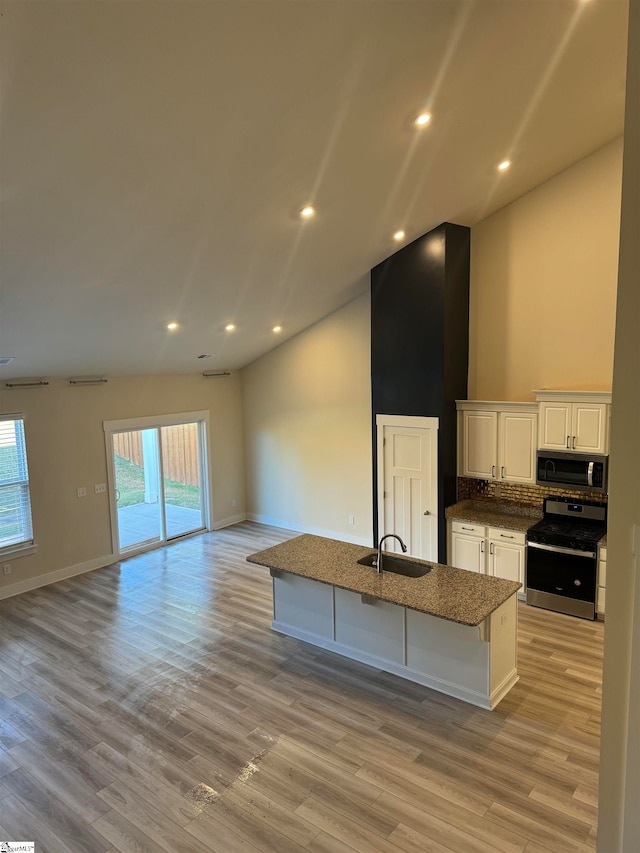 kitchen with a healthy amount of sunlight, appliances with stainless steel finishes, a center island with sink, and white cabinets