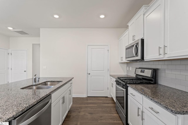 kitchen with appliances with stainless steel finishes, sink, white cabinets, dark stone countertops, and dark hardwood / wood-style floors