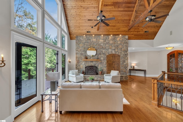 living room with a stone fireplace, beam ceiling, wooden ceiling, light wood-type flooring, and high vaulted ceiling