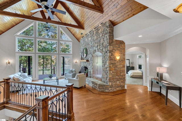 living room featuring wood-type flooring, wood ceiling, a stone fireplace, beam ceiling, and high vaulted ceiling