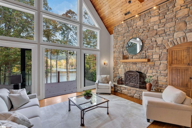 living room featuring light hardwood / wood-style floors, a stone fireplace, high vaulted ceiling, and wooden ceiling