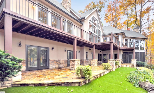 rear view of house with a balcony, french doors, a patio area, and a lawn