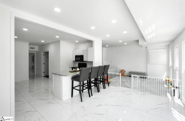 kitchen with white cabinets, light stone countertops, black appliances, and a kitchen bar