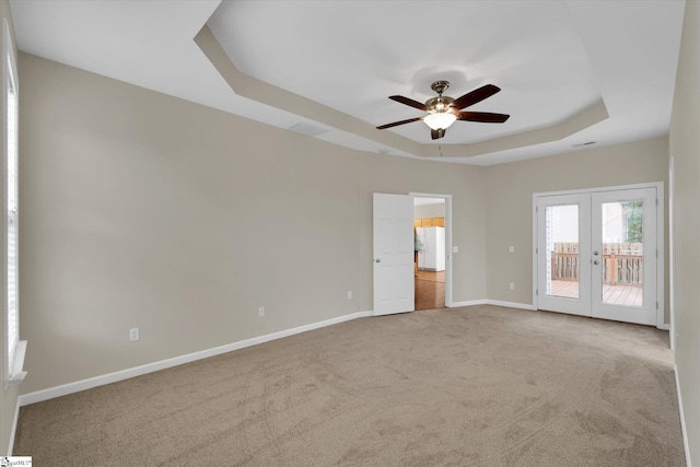 unfurnished room featuring french doors, light colored carpet, a tray ceiling, and ceiling fan